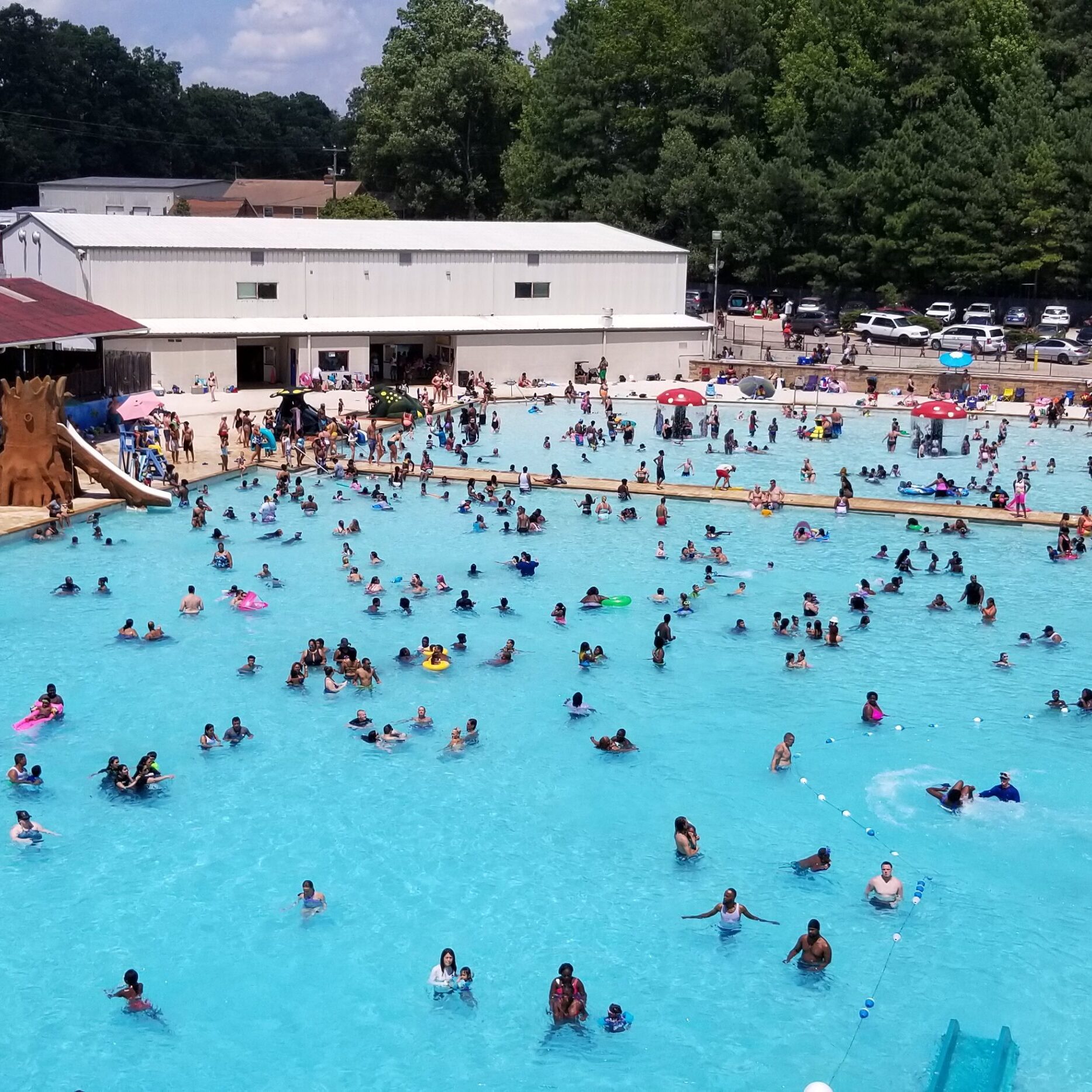 Crowded outdoor swimming pool with many people enjoying the water on a sunny day.